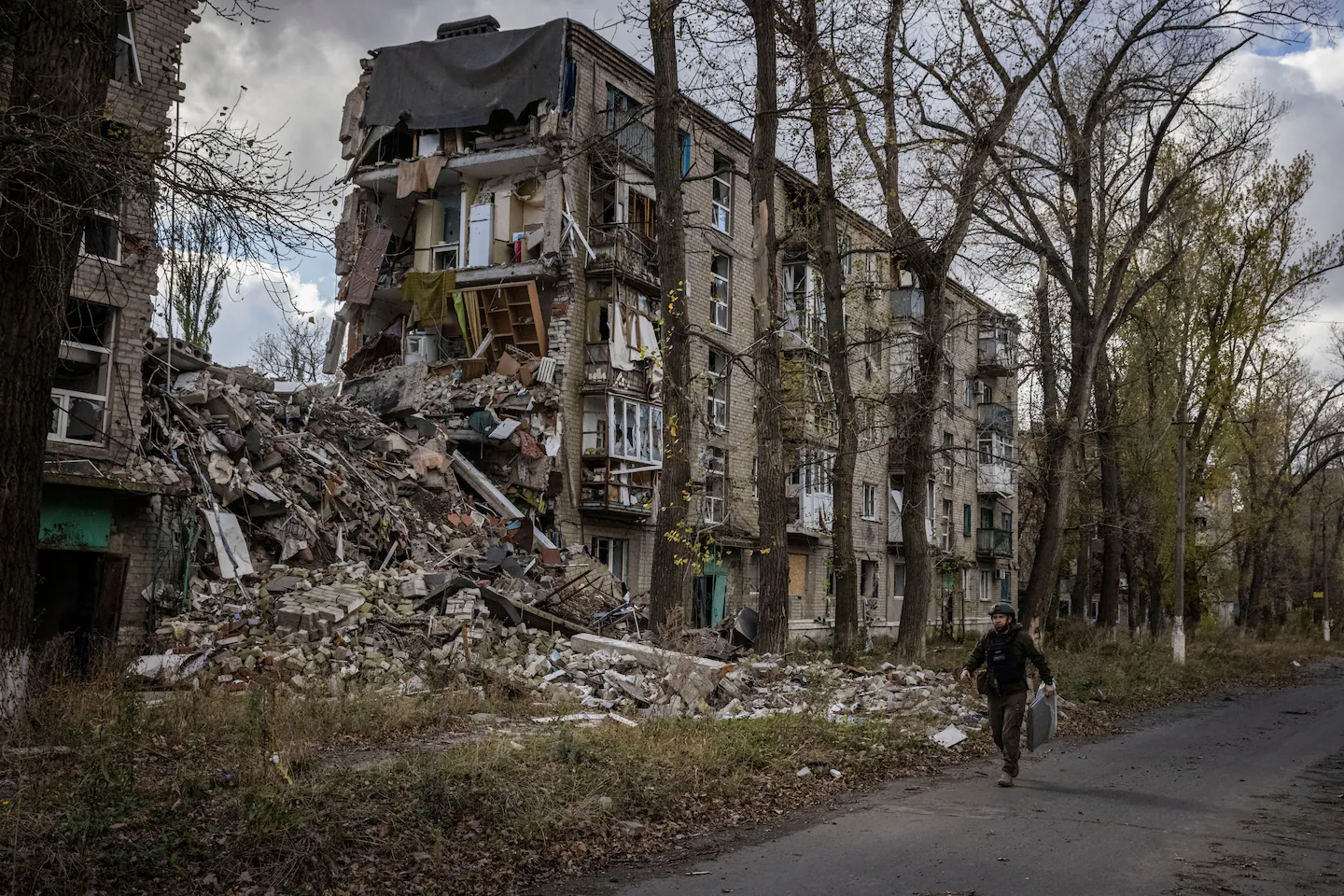 Посадовець з військової адміністрації Авдіївки тримає брезент для доставки та проходить повз зруйновану будівлю, 24 жовтня. Українські сили зазнають посиленого тиску, оскільки російські військові намагаються захопити зруйноване місто